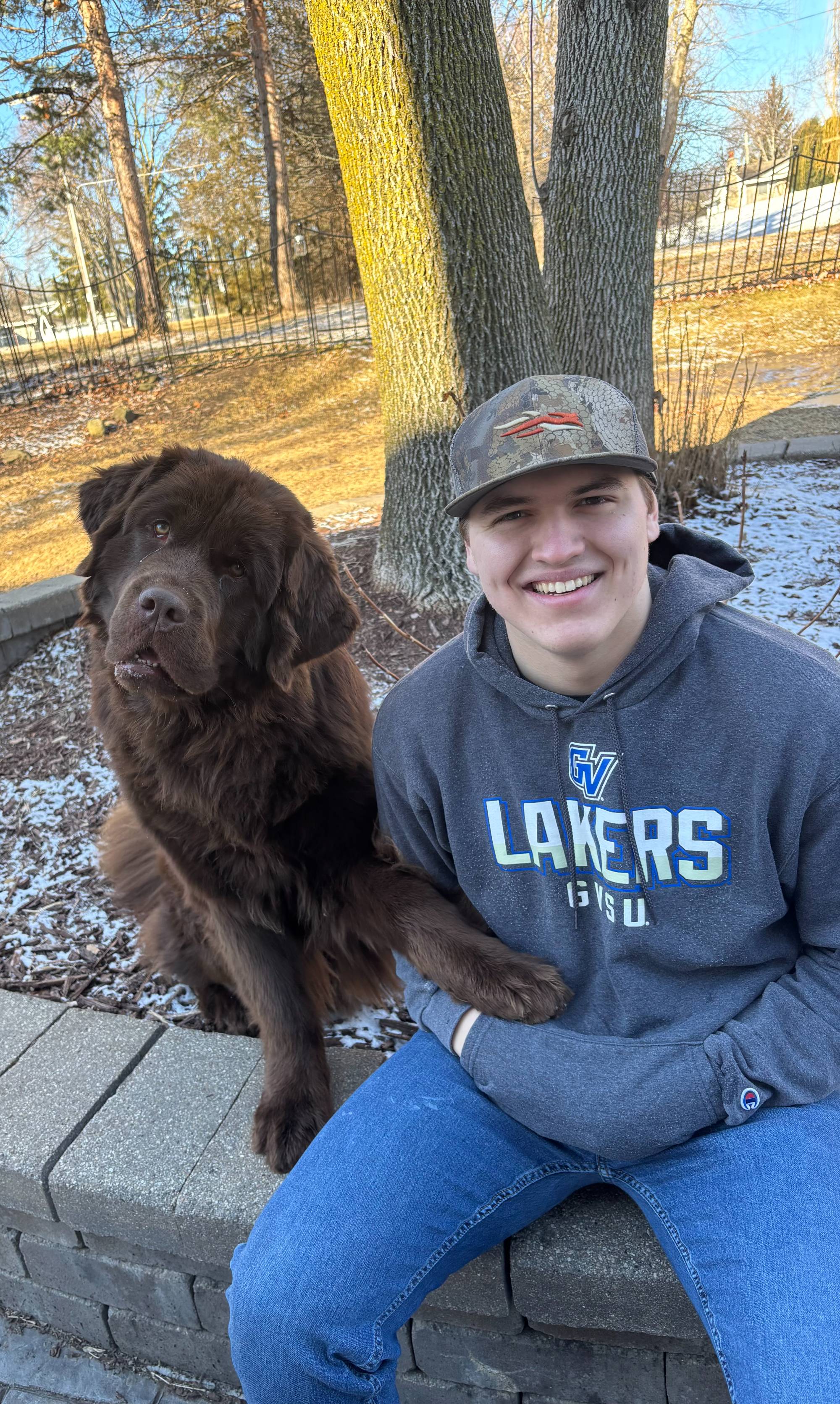young man sitting in front of a tree with his brown dog